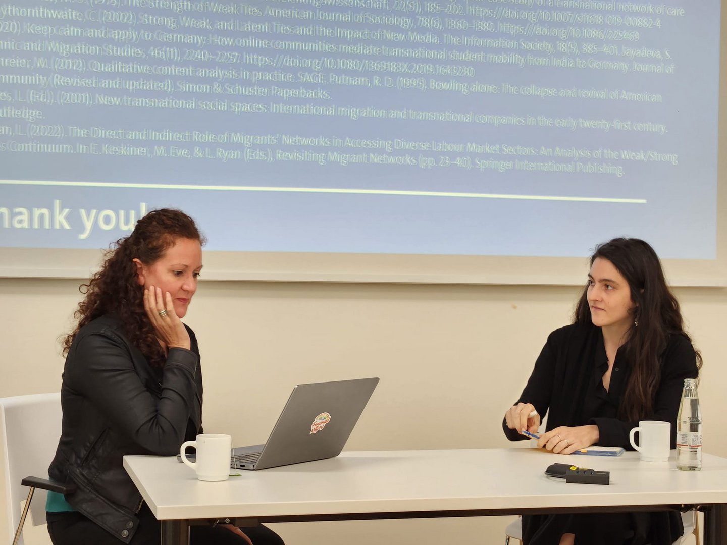 Two women sitting in front of a presentation screen.